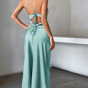 Ljusblå långklänning med snörning och öppning i ryggen  - Supersnygg ljusblå långklänning med smala axelband och öppen rygg med snörningsdetalj. Klänningen har en slimmad passform och är gjord i ett glansigt satinliknande material som ger en lyxig känsla. Perfekt för dig som vill sticka ut med en elegant och modern look.