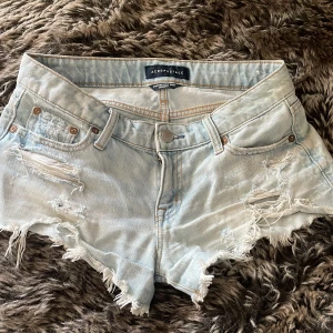 Ljusblå lågmidjade jeansshorts Aeropostale - Säljer ett par ljusblå jeansshorts från Aeropostale med låg midja och råa, fransiga kanter. Shortsen har slitna detaljer och hål både fram och bak, klassiska fickor och dragkedja. Perfekt för dig som gillar en chill och edgy stil.
