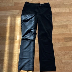 Svarta kostymbyxor med bootcut - Stilrena svarta kostymbyxor med bootcut-snitt och klassisk stängning med knapp och dragkedja. Byxorna har en rak passform upptill och lätt utsvängda ben, perfekta för en clean och dressad look.