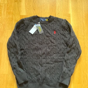 Svart stickad tröja Polo Ralph Lauren - Skriv till mig innan ni köper för jag kan inte frakta på plick så ni får köpa från vinted istället. Kabelstickad svart tröja från Polo Ralph Lauren med klassisk röd broderad logga på bröstet. Tröjan har rund halsringning och långa ärmar, perfekt för lager-på-lager under kyliga dagar. Tillverkad i mjuk bomull för en skön känsla.