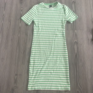 Grön och vit randig kortklänning - Fräsch kortklänning från H&M med gröna och vita ränder. Klänningen har rund hals, korta ärmar och är gjord i mjuk ribbad bomull. Perfekt för dig som gillar en chill och färgglad stil.