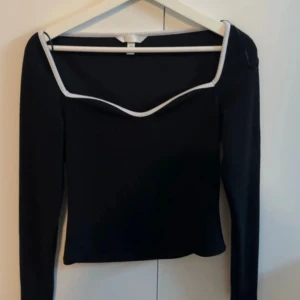 Svart långärmad tröja från H&M - Svart långärmad tröja med urringning från H&M med vit detalj framtill. En tröja som är något kortare i modellen enligt mig, men kan såklart sitta olika på alla. Köpt av en annan tjej på Vinted, endast testad av mig och säljs då den inte passade mig till storleken. Storlek M och för referens pendlar jag mellan M-L och är 168cm lång. 