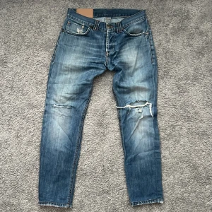 Blå dondup jeans med slitningar  - Snygga blå jeans från Dondup i 100% bomull med slitna detaljer och hål på knäna. Jeansen har raka ben, klassiska bakfickor med dekorativa sömmar och patch med FC-logga bak. Perfekt för dig som gillar en avslappnad och trendig look. Priset går att diskutera
