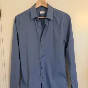 Blå extra slim skjorta Tiger of Sweden - Snygg blå skjorta från Tiger of Sweden i extra slim fit. Skjortan har klassisk krage, långa ärmar och knäppning framtill. Perfekt för dig som gillar en stilren och modern look. Tillverkad i mjuk bomull för skön känsla hela dagen.