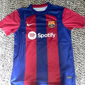 FC Barcelona matchtröja Nike M - Säljer en officiell FC Barcelona matchtröja från Nike i storlek M. Tröjan har klassiska blå och röda vertikala ränder, klubbmärke på bröstet, Nike-logga och Spotify som sponsor. Tillverkad i lätt och ventilerande polyester, perfekt för fotbollsälskare.