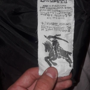 Mer bilder på burberry jackan! - Säljer en svart pufferjacka från Burberry med klassiskt rutigt foder i svart, vitt och rött. Jackan har huva, dragkedja framtill och två fickor. Perfekt för kalla dagar och har en cool streetstil med märkets logga på ärmen.