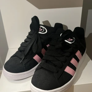 Adidas Campus sneakers svart/rosa - Snygga Adidas Campus sneakers i svart mocka med klassiska tre rosa ränder på sidorna och vit sula. Skorna har svart snörning, säljer då de är för stora för mig💞Aldrig använt bara testade! orginal pris 1200kr