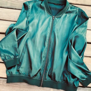 Fin skogsgrön jacka från MyWear! - Fin, kort skogsgrön jacka i satinliknande material med dragkedja & fickor framtill i storlek XL från MyWear. Snygg till fest året om! Sparsamt använd.