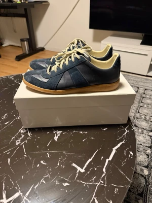 Maison margiela skor - Snygga mörkblå sneakers från maison matgiela med ovandel i mocka och läder, beige snörning och innersida samt klassisk gummisula. Perfekta för dig som gillar retrostil och vill ha något som sticker ut lite extra. Box och dustbags medföljer 