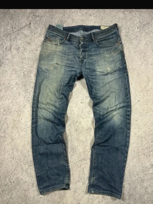 Diesel jeans  - Säljer ett par klassiska blå jeans från Diesel med raka ben och snyggt slitna detaljer framtill. Jeansen har fem fickor, knappgylf och en avslappnad passform. Perfekta för dig som gillar en tidlös och cool stil. Kom förbi vid fundering 