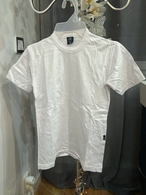 Vit basic t-shirt från Hering Kids - En klassisk vit t-shirt från Hering Kids i mjuk bomull. T-shirten har rund halsringning och korta ärmar, perfekt för en enkel och clean look. Passar till allt och är ett måste i garderoben för dig som gillar stilrena plagg.