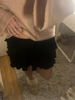 Svart volangkjol med ruffle - Supersöt svart kortkjol med volangdetaljer och ruffle längst ner. Tillverkad i ett mjukt, lätt och skönt material