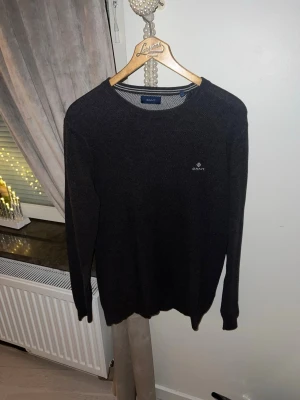 Mörkgrå tröja från Gant - Snygg mörkgrå tröja från Gant med rund halsringning och diskret logga broderad på bröstet. Tröjan har långa ärmar och ribbade muddar vid ärmslut och nederkant. Perfekt till ett stilrent och avslappnat uttryck.