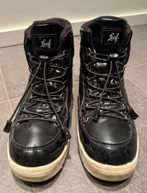Svarta kängor från Leaf med snabb-snörning - Leaf vinter-/höstkängor – stl 38 (unisex)  Säljer ett par svarta vinter/höstkängor från Leaf i storlek 38. Varmfodrade, bekväma och praktiska med snabbsnörning. Passar bra för höst, mild vinter och vardagsbruk.  ✔ Unisexmodell ✔ Varmt innerfoder ✔ Stadig sula med bra grepp ✔ Normalt bruksskick, fullt funktionella  Se bilder för skick.  Pris: 200 kr Pris kan diskuteras vid snabb och smidig affär. Svarta kängor från Leaf med högt skaft och grov vit sula. Kängorna har snörning framtill och är tillv