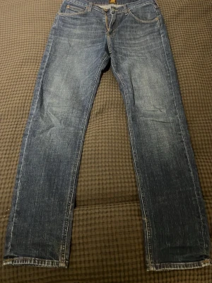 Blå Lee jeans  - Klassiska blå jeans från Lee med raka ben och femficksmodell. Jeansen har en snygg tvättad look och Lee-lapp bak i midjan. Perfekta för dig som gillar tidlös stil och vill ha ett par jeans som funkar till det mesta. Modell: Austin. Storlek: W30 L32. Jeansen är helt nya, inga tecken på användning.