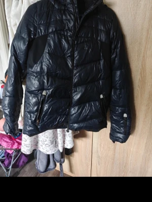 Svart puffer dunjacka med huva Armani,Ea7 - Snygg svart blå dunjacka i puffer-modell med huva och dragkedja framtill. Jackan har två fickor med dragkedja och quiltad design. Perfekt för kalla dagar och ger en modern look.