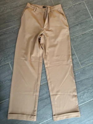 Beige chinos från Gazza - Snygga beige chinos från Gazza med raka ben och klassisk passform. Byxorna har bälteshällor, knapp och dragkedja i gylfen samt två sidofickor. Perfekta för en clean och stilren look. Skiftar till mörk och ljus i färgen beroende på färg. 