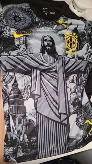 Nike Brasil grafisk fotbollströja - Unik svart och grå fotbollströja från Nike med Brasil-logga och gult swoosh. Tröjan har ett stort grafiskt tryck av Kristusstatyn och detaljerade illustrationer över hela framsidan. Perfekt för dig som vill sticka ut på planen.