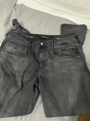 Grå Replay An sopass jeans - Säljer ett par grå Replay Anbass jeans med klassisk femficksdesign och dragkedja. Jeansen har en snygg tv sopad finish och är tillverkade i mjukt bomullsmaterial med lite stretch för extra komfort. Perfekta för dig som gillar en modern och avslappnad stil.. 33/30