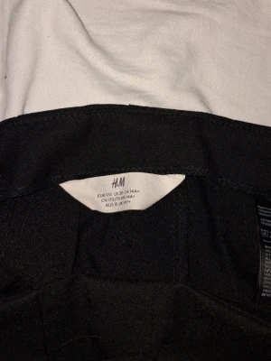 Svart kortkjol från H&M - Snygg svart kortkjol från H&M med utställd form och diskreta veck framtill. Kjolen har en enkel och stilren design som passar till många olika looks. Perfekt för dig som gillar klassiska plagg med en modern twist.