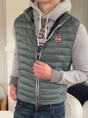 Grön dunväst från Colmar - Snygg grön dunväst från Colmar med quiltad design och dragkedja framtill. Västen har två sidofickor med dragkedja och en rund Colmar-logga på bröstet. Perfekt att slänga över en hoodie för en avslappnad och trendig look.