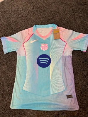 Nike FC Barcelona matchtröja blårosa - Snygg FC Barcelona matchtröja från Nike i ljusblått med rosa och vita detaljer. Tröjan har klubbmärke och Nike-logga på bröstet samt Spotify-logga i mitten. Tillverkad i lätt och ventilerande funktionsmaterial, perfekt för träning eller match. Storlek S