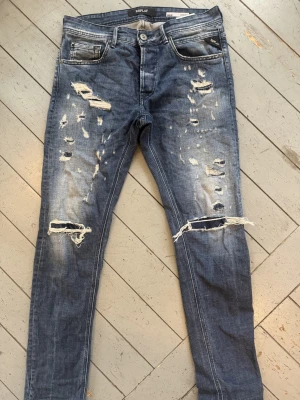Blå slitna Replay jeans skinny fit - Säljer ett par blå  jeans från Replay med slitningar och hål på knäna. Jeansen har klassisk , låg midja och tydliga slitingar framtill. Bara använda ett fåtall gånger