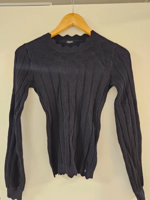 Mörkblå ribbstickad tröja Guess - Snygg mörkblå stickad tröja från Gina Tricot med ribbstickat mönster och dekorativ strukturstickning upptill. Tröjan har rund halsringning och långa ärmar. Perfekt för lager på lager och enkel att matcha med jeans eller kjol.