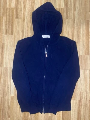 Mörkblå hoodie med dragkedja - En enkel och stilren mörkblå hoodie med dragkedja framtill och huva. Hoodien har långa ärmar och ribbade muddar vid ärmslut och nederkant. Perfekt för en avslappnad look och passar till det mesta i garderoben.