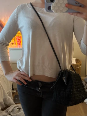 Svart handväska i syntetmaterial - Snygg svart handväska med axelrem och mjuk, fluffig textur. Väskan har en enkel och stilren design som passar till många outfits. Perfekt storlek för det viktigaste och lätt att bära både på axeln och i handen.