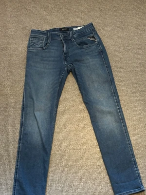 Blå Replay jeans  - Snygga blå Replay Anbass jeans med klassisk femficksdesign och diskreta slitningar. Jeansen har slim passform och är tillverkade i mjukt denimtyg med stretch för extra komfort. Bakfickorna har Replay-logga och coola sömdetaljer.