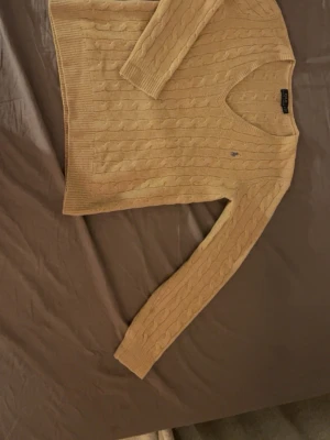 Ralph Lauren ljusbrun tröja - Säljer en ljusbrun tröja med v-ringning. Loggan är broderad i lila (äkta)💜Det kan se gult ut på bilderna men är ej det i verkligheten, när den sitter på kroppen upplevs tröjan som storlek M!