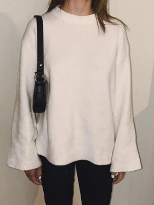 Svart axelväska med gulddetalj - Säljer en stilren svart axelväska med guldfärgad metallring och logga framtill. Väskan har en smal axelrem och minimalistisk design som gör den enkel att matcha till olika outfits. Perfekt storlek för det viktigaste och tillverkad i ett slätt material. Helt i nyskick