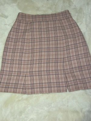 Rutig rosa kortkjol i bomull - Supersnygg rutig kortkjol i rosa och beige toner. Kjolen har en klassisk A-linjeform och små slitsar framtill. Perfekt för dig som gillar preppy stil och vill ha något som sticker ut. Tillverkad i mjuk bomull som känns skön mot huden.