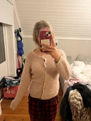 Beige fluffig kofta med knappar - Mysig beige kofta med fluffig textur och rund halsringning. Koftan har långa ärmar och stängs med små knappar framtill. Perfekt för lager-på-lager och en chill look.