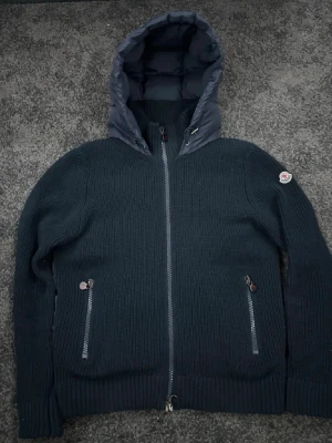 Mörkblå teddyjacka från Moncler - Snygg mörkblå teddyjacka från Moncler med stickade ärmar och vadderad huva samt rygg. Jackan har dragkedja framtill och två fickor med dragkedja. Moncler-logga på ärmen. Perfekt för kyliga dagar.