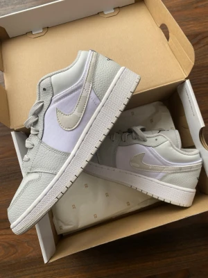 Nike Jordan 1 Low i grå och vit - Snygga Nike Air Jordan 1 Low sneakers i vit och ljusgrå färg. Skorna är använda vid väldigt få tillfällen och är i mycket fint skick. Inga crease-märken alls. Originalbox medföljer och kvitto finns för att styrka äktheten.  Hör av dig vid frågor eller fler bilder