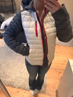 Grå och vit dunjacka från DR.Zipe  - Snygg dunjacka från i vitt och mörkgrått med röda dragkedjor. Jackan har huva, lång ärm och quiltad design framtill. Perfekt för kalla dagar och har en sportig vibe. Jackan har små svarta fläckar på ryggen, går förmodligen bort i tvätten eller med någon bra rengöringssprej. Har själv inte testat då den inte kommer till användning. 