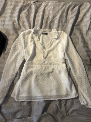 Vit blus med volang och prickar - Söt vit blus från SHEIN med volangkant vid halsringningen och små prickar i tyget. Blusen har lång ärm och knäppning framtill. Perfekt för en trendig och feminin look.