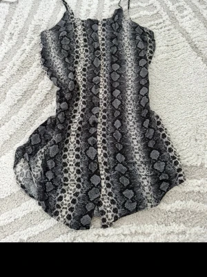 Svart och vit linnetopp från H&M Divided - Snygg linnetopp från H&M Divided i svart och vitt med ormmönster. Toppen är ärmlös med tunna axelband och har en lätt och luftig känsla, perfekt för varma dagar. Materialet är mjukt och följsamt.