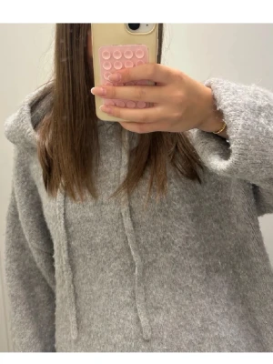 Grå fluffig hoodie med dragsko - Mysig och oversized hoodie i ljusgrå färg med fluffigt material. Hoodien har huva med dragsko och långa ärmar med ribbade muddar. 