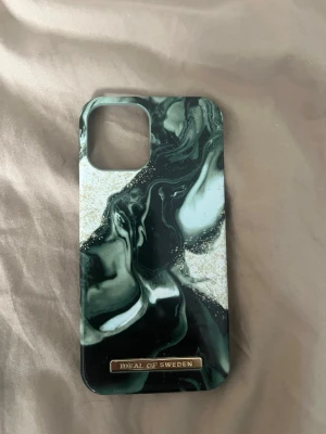 Marmorerat mobilskal Ideal of Sweden iPhone 12 - Snyggt mobilskal med marmorerat mönster i grönt, svart, vitt och inslag av guld. Skalets material är hårdplast och det har en elegant metallbricka med loggan längst ner. Passar perfekt för dig som vill ha en stilren look på mobilen. iPhone 12
