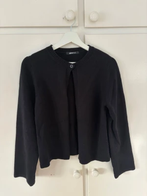 Svart kofta från Gina Tricot - En svart, enkel stickad kofta från Gina Tricot med rund halsringning och en knapp framtill. Koftan har långa ärmar och ribbade kanter vid hals och ärmslut. Storlek M🩷