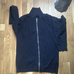 Mörkblå ziptröja med hög krage - Snygg mörkblå jack and jones ziptröja med hög krage och hel dragkedja framtill. Tröjan är ribbstickad och har långa ärmar. Perfekt för lager på lager och enkel att matcha med olika outfits. Den är stor i storleken 