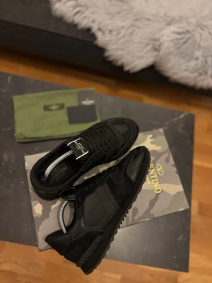 Svarta rockrunners från Valentino - Snygga svarta sneakers från Valentino med klassisk siluett. Skorna har ovandel i mocka och skinn. De är knappast använda och i oerhört bra skick. De kommer med påser och kort ifrån valentino. Även boxen. De är i storlek 43 och är varken små eller stora i storleken utan helt perfekta.
