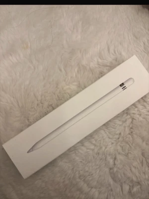 Apple Pencil (1st Gen) stylus - Säljer en Apple Pencil (1st Gen) i vitt. Den är tillverkad i slät plast och har en elegant, smal design med silverdetaljer vid toppen. Perfekt för att rita, anteckna eller redigera på din iPad. Kommer i originalförpackning. Fick i present därav säljer den efterson har en annan penna
