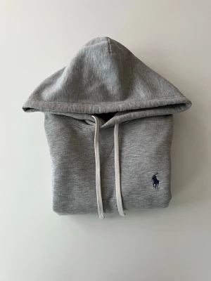 Grå Polo Ralph lauren hoodie  - Grå hoodie från Polo Ralph Lauren i storlek XS. Klassisk och stilren modell med huva, snörning och broderad Polo logga på bröste. Mjuk och bekväm och väldigt skön att bära. Hoodien är i mycket fint skick utan hål eller andra synliga defekter. Den passar perfekt nu till lite kyligare väder, både till vardags och en mer avslappnad stil. Om du har frågor eller funderingar hjälper jag gärna till Mvh Olof.
