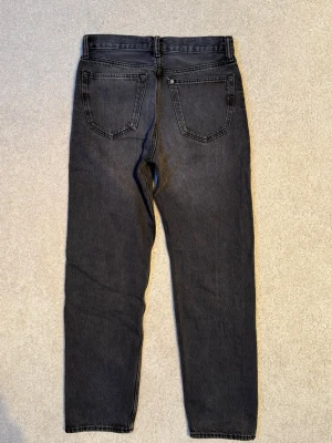 Svarta raka H&M jeans med normalhög midja  - Säljer ett par svarta H&M jeans med normalhög midja och raka ben. Jeansen har klassisk femficksdesign och har en knappgylf. Materialet är jeans i bomull.