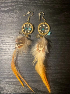 Coola örhängen❤️ - Super fina lrhängen som påminner om drömmfångare❤️jag köpte dom ifrån en kvinna som gjorde dom själv i sydamerika❤️tyvärr är ena örhängets fjädrar lite trasiga som man kan se på bilderna❤️ de är små turkos ädelsenar på❤️