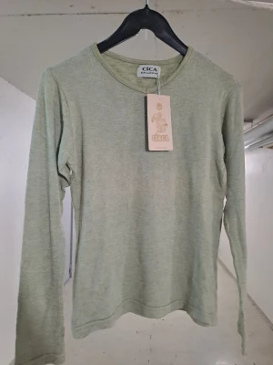 Ljusgrön långärmad topp från Cica - En stilren ljusgrön långärmad topp från Cica. Toppen har rund halsringning och är tillverkad i ett mjukt, ribbat material som ger en bekväm passform. Perfekt att matcha med jeans eller kjol för en enkel och snygg look.